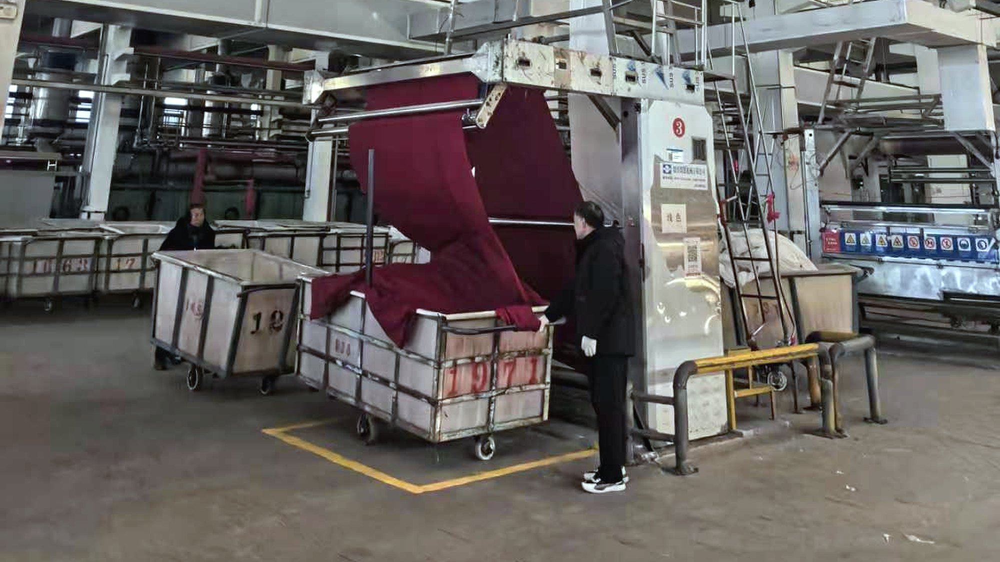 Deep red knitted fabric running out of a dyeing machine on a partner factory floor in China.
